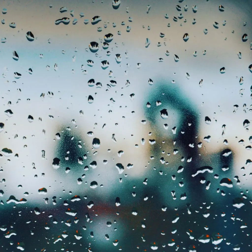 Raindrops on a window with a blurred city background, symbolizing the need for marketing clarity and focus amid changing conditions.